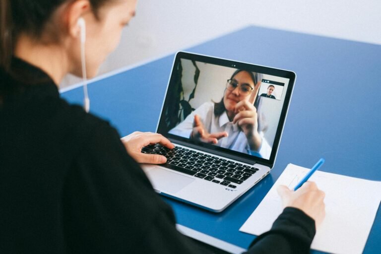 Mujer participando en una reunión virtual, tomando notas durante una videoconferencia en una computadora portátil.